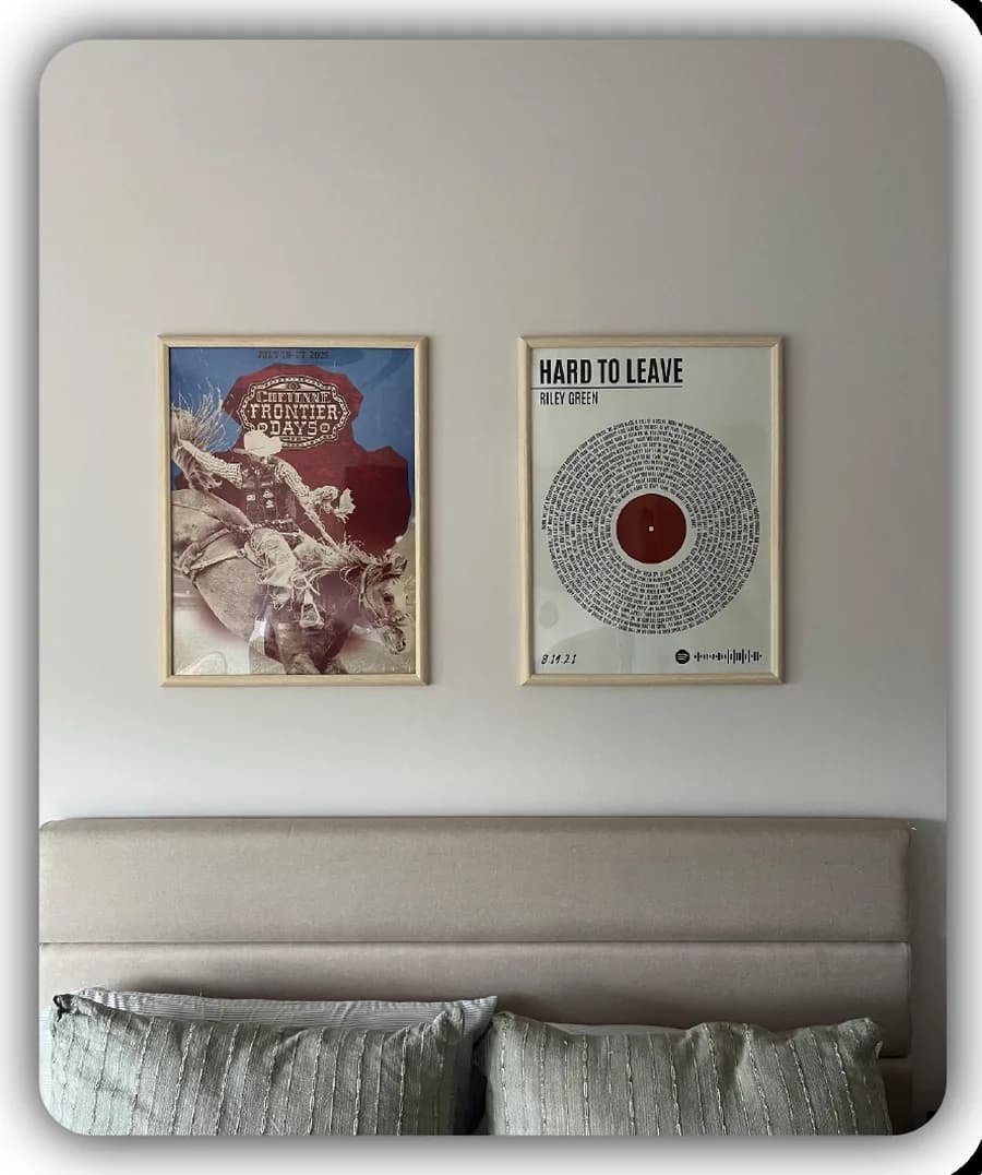Two framed prints hung side by side above a bed: a rodeo poster and a Hard to Leave lyric print by Riley Green laid out as a vinyl record.
